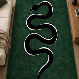 May include: A rectangular area rug featuring a deep forest green background with a large, stylised black snake graphic winding through the centre. The snake is outlined in a bold white border, creating a high-contrast design across the surface.