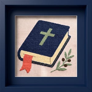 May include: A cross-stitch embroidery featuring a dark blue book with a light green cross on the cover, a cream-coloured page edge, and a red ribbon bookmark. An olive branch with small dark berries sits beside the book on a light pink fabric.