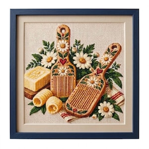 May include: A framed cross-stitch embroidery featuring two wooden butter paddles decorated with embroidered white daisies and small red hearts, accompanied by a block of butter, two butter curls, and a striped cloth, all set against a beige fabric.