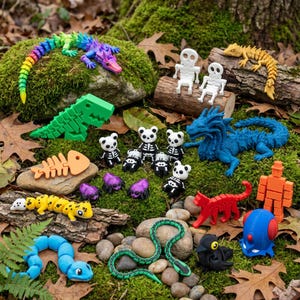 May include: A collection of articulated 3D printed figures including a rainbow lizard, a green dinosaur, a blue dragon, a yellow gecko, a blue snake, a red cat, a black bird, a blue robot, and several small panda skeletons and purple spiders.