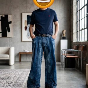 以下が含まれることがあります： 胸元に小さな赤いロゴが入ったネイビーブルーの半袖Tシャツ。フロントにダークウォッシュのパネルが施されたワイドレッグのブルージーンズと、円形のバックルが付いたダークブラウンのレザーベルトを合わせ、ブラウンのスエードシューズを着用。