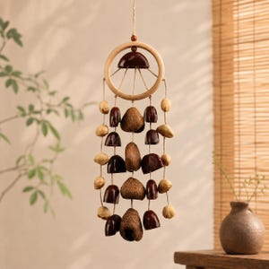 May include: A hanging wind chime featuring a wooden ring and a series of hanging natural elements. The chime includes dark brown, light brown, and beige components, suspended by twine. The design is simple and natural, suitable for indoor or outdoor decor.