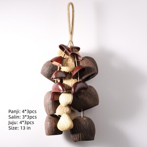May include: A decorative hanging ornament featuring natural materials. The design includes dark brown coconut shells, light brown seed pods, and small, reddish-brown bell-shaped pieces. The ornament is approximately 13 inches in length and is suspended by a natural fiber rope.