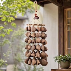May include: A hanging wind chime made of natural brown coconut shells. The chime is suspended from a woven rope and features a wooden frame. The shells are arranged in multiple rows, creating a decorative and organic design.