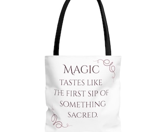 Puede incluir: Un bolso tote blanco con asas negras que presenta el texto en color morado oscuro MAGIC TASTES LIKE THE FIRST SIP OF SOMETHING SACRED. El diseño incluye delicados adornos en espiral de color morado en las esquinas superior derecha e inferior izquierda.