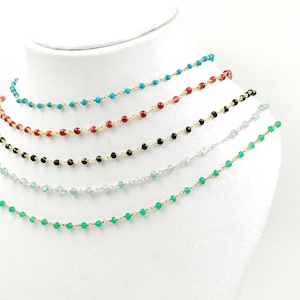 Puede incluir: Exhibición de delicados collares de cuentas en varios colores, incluyendo turquesa, rojo, negro, azul claro y verde. Cada collar presenta pequeñas cuentas coloridas ensartadas en una fina cadena, mostrando un diseño minimalista. Los collares se exhiben en un busto de maniquí blanco.