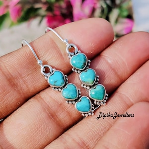 May include: Silver earrings with turquoise heart-shaped stones. Each earring has three heart-shaped stones in a vertical line, connected by silver links. The earrings have a hook closure. The text "Dipika Jewellers" is visible on the bottom right.