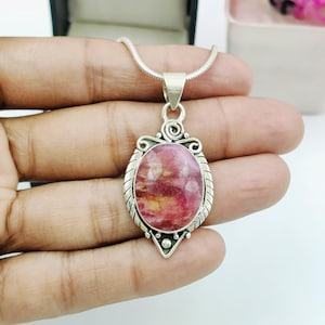 Può includere: Una collana con pendente in argento caratterizzata da una gemma ovale sfaccettata rosa e gialla, incastonata in una cornice d'argento decorativa con dettagli a voluta sulla parte superiore e una base a punta, su una sottile catena a serpente.