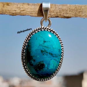 Può includere: Ciondolo ovale con una vibrante pietra turchese, incastonato in una cornice in metallo argentato con un bordo a forma di corda. Il ciondolo è appeso a un'ansa d'argento. Il testo "dipikajwellers" è visibile.