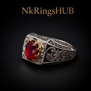 May include: A silver ring featuring an oval-cut red gemstone set in a gold-toned bezel, surrounded by small clear stones. The band displays intricate black engraved scrollwork patterns. The text NkRingsHUB is visible above the ring.