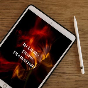 Può includere: Un tablet bianco con bordo nero mostra un design astratto rosso e arancione infuocato su sfondo nero. Il testo "IN LIEBE - DEINE DUNKELHEIT" è scritto in bianco. Una penna bianca è appoggiata accanto al tablet su una superficie di legno.