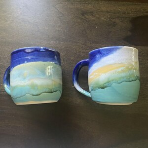 May include: Two ceramic mugs with a blue, white, and green glaze. The mugs have a rounded shape and a handle.