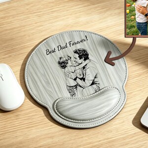 May include: A round mouse pad with a light grey wood grain pattern featuring a black and white line art illustration of a person hugging a child. The text "Best Dad Forever!" is printed above the illustration, and a wrist rest is attached.