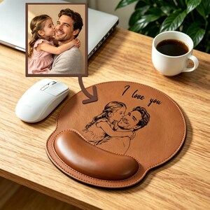 May include: A tan leather mouse pad with a wrist rest, featuring a custom laser-engraved illustration of a child kissing a parent on the cheek. The text "I love you" is engraved above the illustration, which is based on the inset photo.