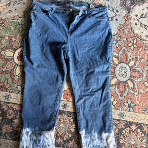 K&ouml;nnte beinhalten: Blaue Jeans mit einem Batik-Effekt an den Manschetten. Die Jeans haben ein klassisches F&uuml;nf-Taschen-Design und einen Knopf- und Rei&szlig;verschluss. Der Denim hat eine mittlere Waschung, und der Batik-Effekt ist wei&szlig; und blau.