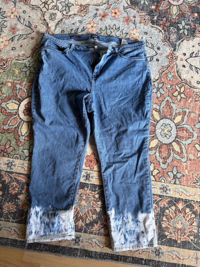 K&ouml;nnte beinhalten: Blaue Jeans mit einem Batik-Effekt an den Manschetten. Die Jeans haben ein klassisches F&uuml;nf-Taschen-Design und einen Knopf- und Rei&szlig;verschluss. Der Denim hat eine mittlere Waschung, und der Batik-Effekt ist wei&szlig; und blau.