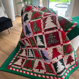 Könnte beinhalten: Eine Patchwork-Decke mit einem Raster aus quadratischen Blöcken, die jeweils ein anderes Weihnachtsbaum-Motiv in verschiedenen Rot-, Grün-, Weiß- und Schwarztönen zeigen. Die Decke ist mit einem grünen Rand und einer rot-weiß gestreiften Borte versehen.
