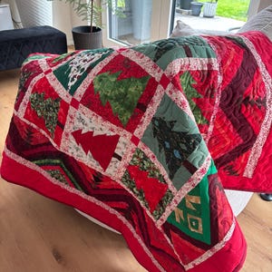 May include: A patchwork quilt featuring a repeating pattern of Christmas tree motifs in various shades of green, red, and white. The quilt is constructed with square blocks separated by thin white fabric strips and finished with a solid red border.