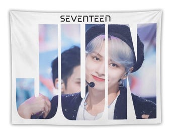 May include: White wall tapestry featuring the word "SEVENTEEN" above the name "JUN" in large, vertical letters. The image behind the letters shows a person with light blue hair wearing a black beret and jacket.