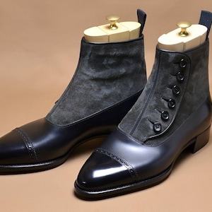 May include: A pair of black leather ankle boots with gray suede panels. The boots have a button closure and a pointed toe. Wooden shoe trees are inserted in the boots.