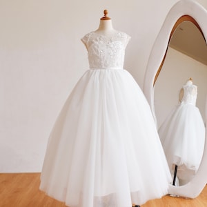 Può includere: Abito bianco in tulle su manichino, con corpetto ricamato e gonna ampia. L'abito è esposto davanti a uno specchio, che riflette il design. Adatto per occasioni speciali.