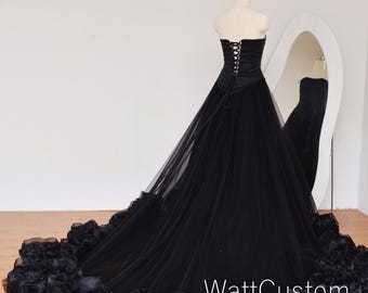 May include: A strapless black gown with a corset bodice and a flowing tulle skirt. The skirt is embellished with large, satin rosettes at the hem. The text "WattCustom" is visible on the skirt.