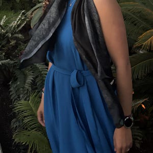 K&ouml;nnte beinhalten: Ein &auml;rmelloses, kobaltblaues Kleid mit passendem G&uuml;rtel. Ein schwarz-grau gemusterter Schal ist &uuml;ber den Schultern drapiert. Eine schwarze Armbanduhr ist am Handgelenk zu sehen.