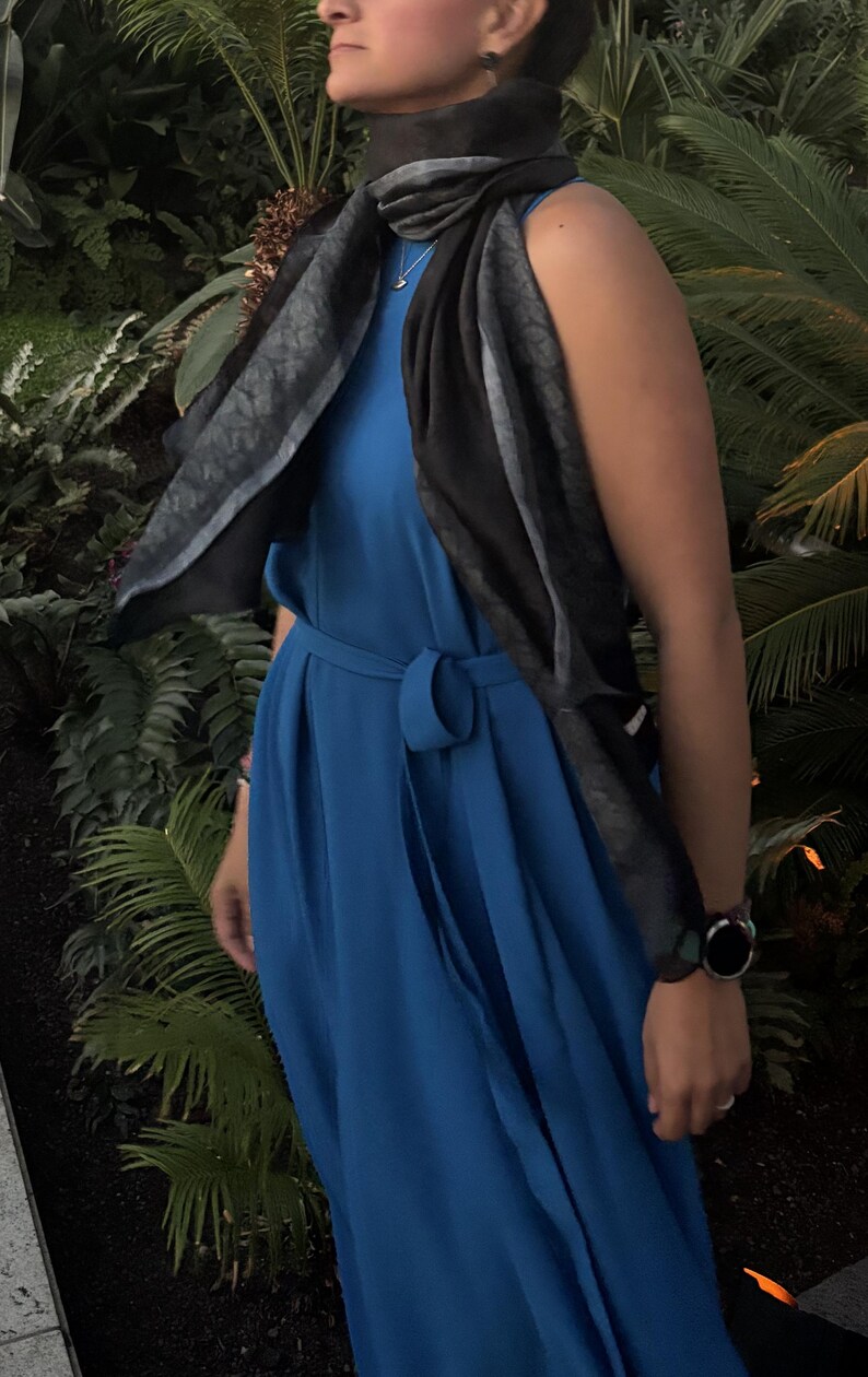 K&ouml;nnte beinhalten: Ein &auml;rmelloses, kobaltblaues Kleid mit passendem G&uuml;rtel. Ein schwarz-grau gemusterter Schal ist &uuml;ber den Schultern drapiert. Eine schwarze Armbanduhr ist am Handgelenk zu sehen.