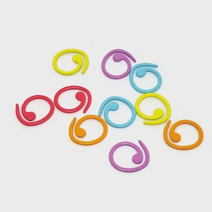 May include: A selection of multi-coloured spiral stitch markers. The markers are in shades of red, orange, yellow, blue, and purple. These small, curved markers are used for knitting and crochet projects.