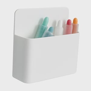 May include: A white, wall-mounted organizer with a rectangular shape and a raised back. It contains several colorful, cylindrical objects in shades of blue, white, pink, and orange. The organizer is made of smooth, solid white plastic.