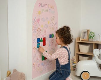 May include: A tall, arched, light pink wall decal featuring the text PLAY TIME and various colorful hand-drawn illustrations like hearts, stars, and figures. Several small, translucent, geometric magnetic tiles are attached to the surface.