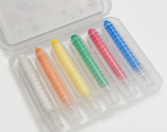 May include: A clear plastic case containing six colorful crayons. The crayons are white, orange, yellow, green, red, and blue. Each crayon has a clear plastic casing and a white tip. The case is open, revealing the crayons inside.
