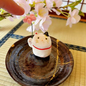 May include: A set of three ceramic mugs with a speckled, matte finish. The mugs are in shades of cream, light gray, and dark gray. Each mug has a simple, minimalist design and a rounded handle.