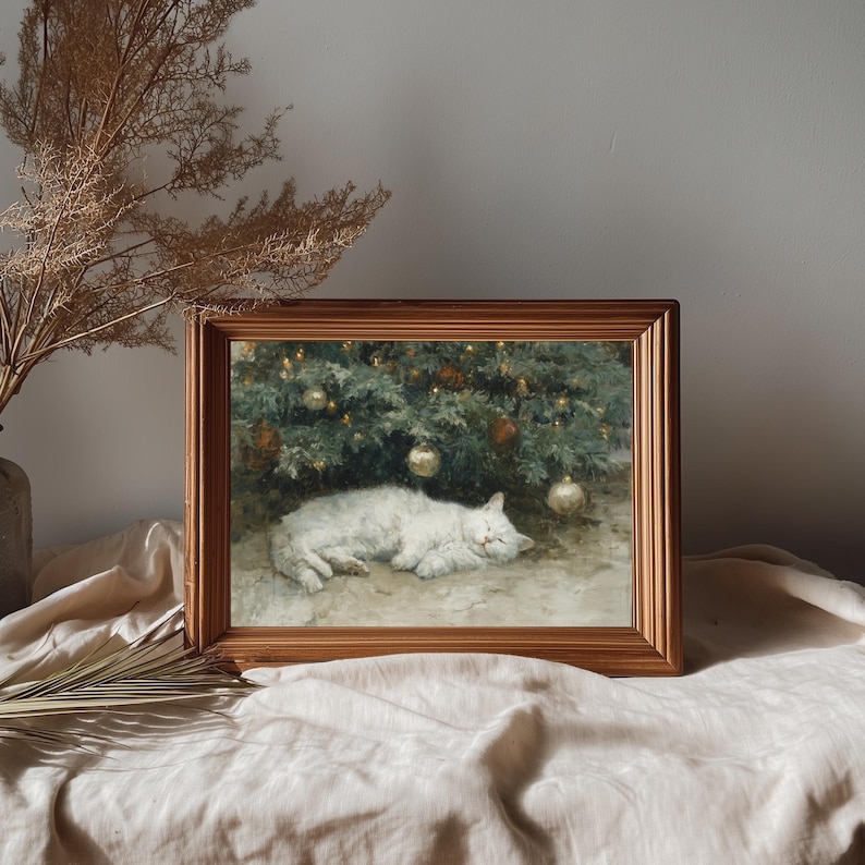 May include: A framed print depicts a sleeping white cat under a decorated Christmas tree. The artwork has a vintage aesthetic, with soft lighting and warm tones. The frame is a warm brown color, adding to the cozy feel.
