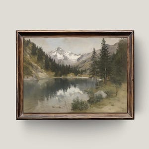 May include: A framed landscape painting depicts a serene mountain lake scene. The artwork features snow-capped mountains, evergreen trees, and a reflective lake, all under a cloudy sky. The frame is a dark wood.