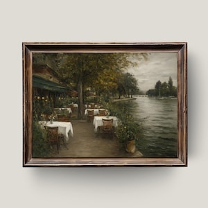 Op de afbeelding: Een ingelijst olieverfschilderij toont een café aan het water. Tafels met witte tafelkleden en rieten stoelen staan opgesteld langs een pad. Bomen met gele en groene bladeren staan langs het pad. Een rivier en een bewolkte lucht zijn op de achtergrond.