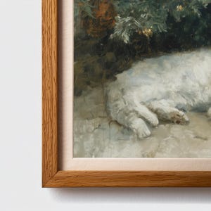 May include: A framed painting depicts a white cat resting in a garden setting. The artwork features a light brown wooden frame and a soft, neutral-toned mat. The cat's fur is rendered in shades of white and gray, with hints of pink on its paws.