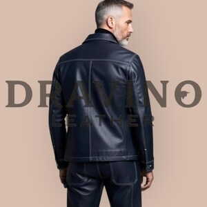 May include: A navy blue leather jacket and matching pants with white stitching. The jacket has a collar and buttoned cuffs. The text "DRAVINO LEATHER" is printed on the image. The outfit is worn by a person.