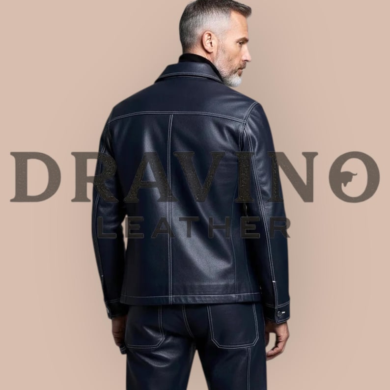 May include: A navy blue leather jacket and matching pants with white stitching. The jacket has a collar and buttoned cuffs. The text "DRAVINO LEATHER" is printed on the image. The outfit is worn by a person.