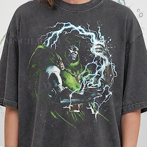 May include: Dark gray t-shirt featuring a comic book illustration of a character in a green cloak, with a lightning bolt design. The text "PEPPER COMFORT COLORS" is printed at the bottom of the shirt.