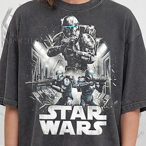 May include: Dark gray t-shirt featuring a Star Wars graphic. The design includes images of soldiers in helmets and the Star Wars logo in white. The text "Pepper Comfort Colors" is at the bottom.