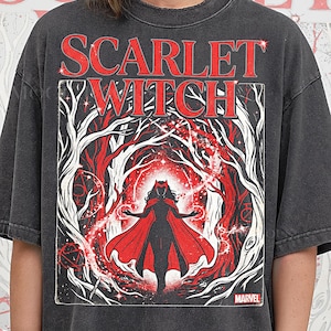 May include: Dark grey t-shirt with a graphic of Scarlet Witch, featuring red text and imagery. The design includes the words "SCARLET WITCH" and a Marvel logo. The artwork depicts a figure in a red cape surrounded by a red and white forest.