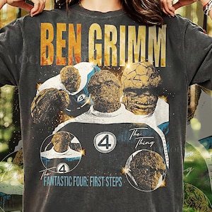 May include: Dark gray t-shirt featuring a distressed graphic of Ben Grimm, also known as The Thing, from The Fantastic Four. The design includes the text "BEN GRIMM" and "The Fantastic Four: First Steps".