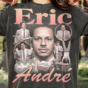 May include: A charcoal gray t-shirt featuring a large graphic print of Eric Andre. The design includes multiple images of the comedian, a stack of books labeled "LEGALIZE EVERYTHING," bottles of ranch dressing, and the name "Eric Andre" in pink.