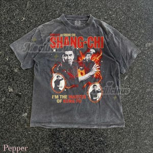 以下が含まれることがあります： 「SHANG-CHI」の赤い文字とキャラクターの画像が特徴のチャコールグレーのTシャツ。「I'M THE MASTER OF KUNG FU」というフレーズも含まれています。