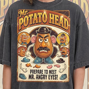 Könnte beinhalten: Dunkelgraues T-Shirt mit einem Vintage-Mr. Potato Head-Motiv. Das Design zeigt die Worte "Mr. Potato Head" in einer Retro-Schriftart, verschiedene Mr. Potato Head-Teile und den Satz "Prepare to meet Mr. Angry Eyes!"