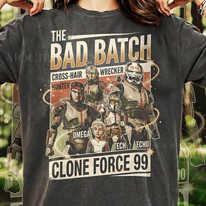 May include: Dark gray t-shirt featuring a graphic of the Bad Batch from Clone Force 99. The design includes the text "THE BAD BATCH" and character names like Crosshair, Hunter, Wrecker, Omega, Tech, and Echo. The shirt is printed with Pepper Comfort Colors.