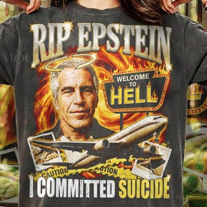 Op de afbeelding: Donkergrijs t-shirt met een grafisch ontwerp. Het ontwerp bevat de tekst "RIP EPSTEIN", een portret, een bord met de tekst "WELCOME TO HELL", een vliegtuig en de tekst "I COMMITTED SUICIDE".