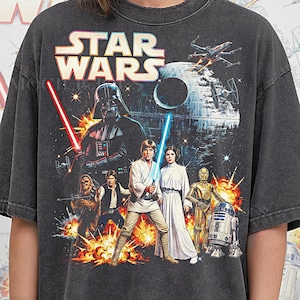 Pode incluir: T-shirt cinzento escuro com gráfico de Star Wars com Darth Vader, Luke Skywalker, Princesa Leia e outros personagens. A camisa tem o texto "STAR WARS" na parte superior e "PEPPER COMFORT COLORS" na parte inferior.