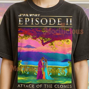 May include: Dark gray t-shirt featuring a colorful graphic from Star Wars: Episode II - Attack of the Clones. The graphic shows a couple in front of a lake with a vibrant sunset. The text "STAR WARS EPISODE II" is at the top.